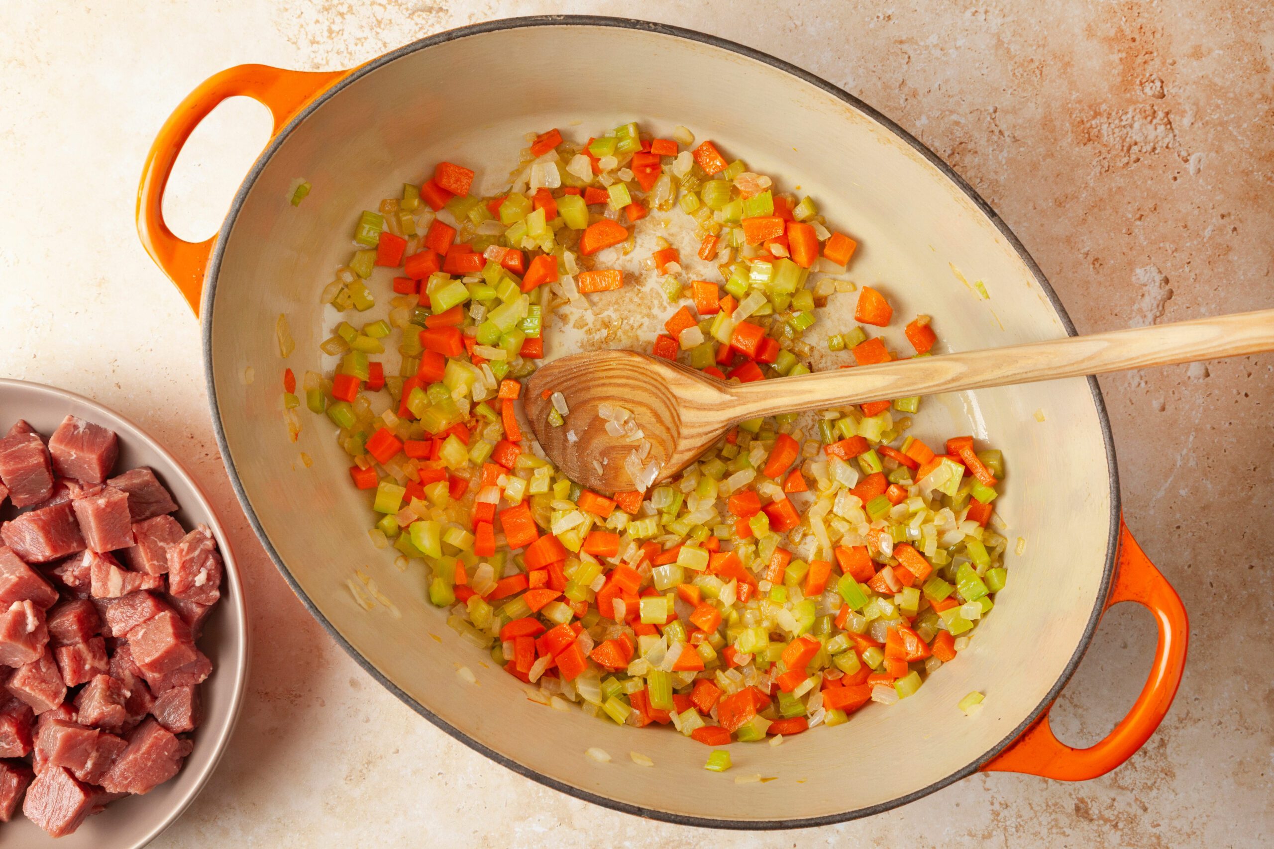 Colorful mixture of diced vegetables is sautéed, a wooden spoon rests among the vegetables