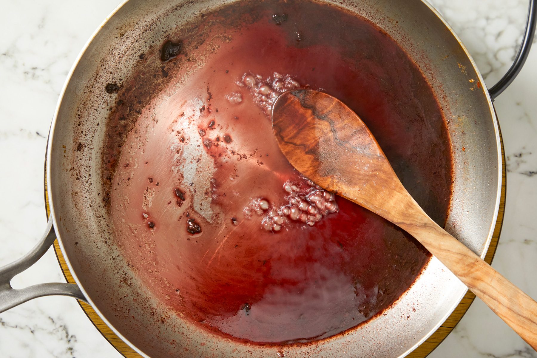 Red wine poured into hot skillet, deglazing with wooden spoon, then poured over roast in slow cooker.