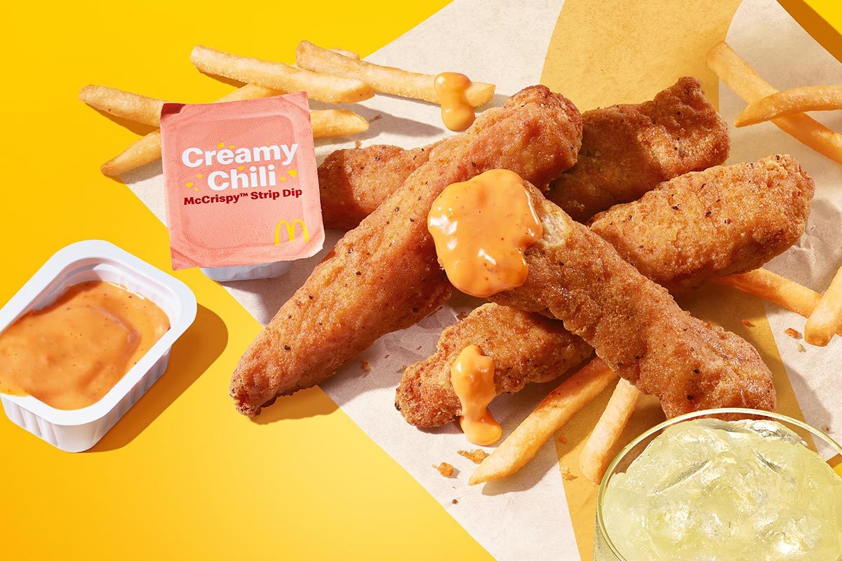 Stack of McDonald's chicken strips dipped in pink sauce with french fries and lemonade on a yellow background