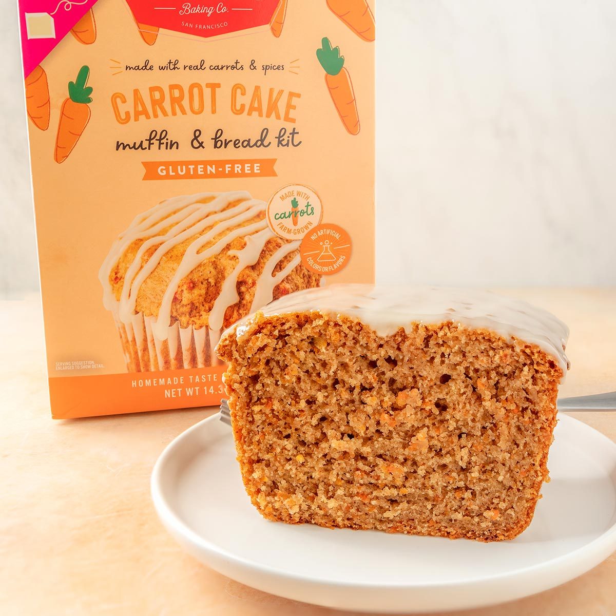 Miss Jones slice of carrot cake with cream cheese frosting on a white plate with the box in the background