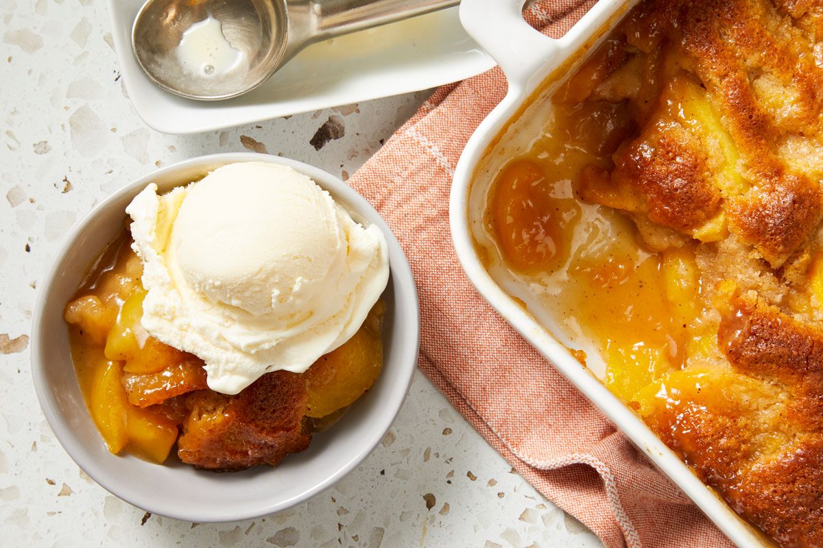 Overhead shot of Tennessee Peach Pudding; in a baking pan over napkin; served in a bowl top with ice cream; marble surface;