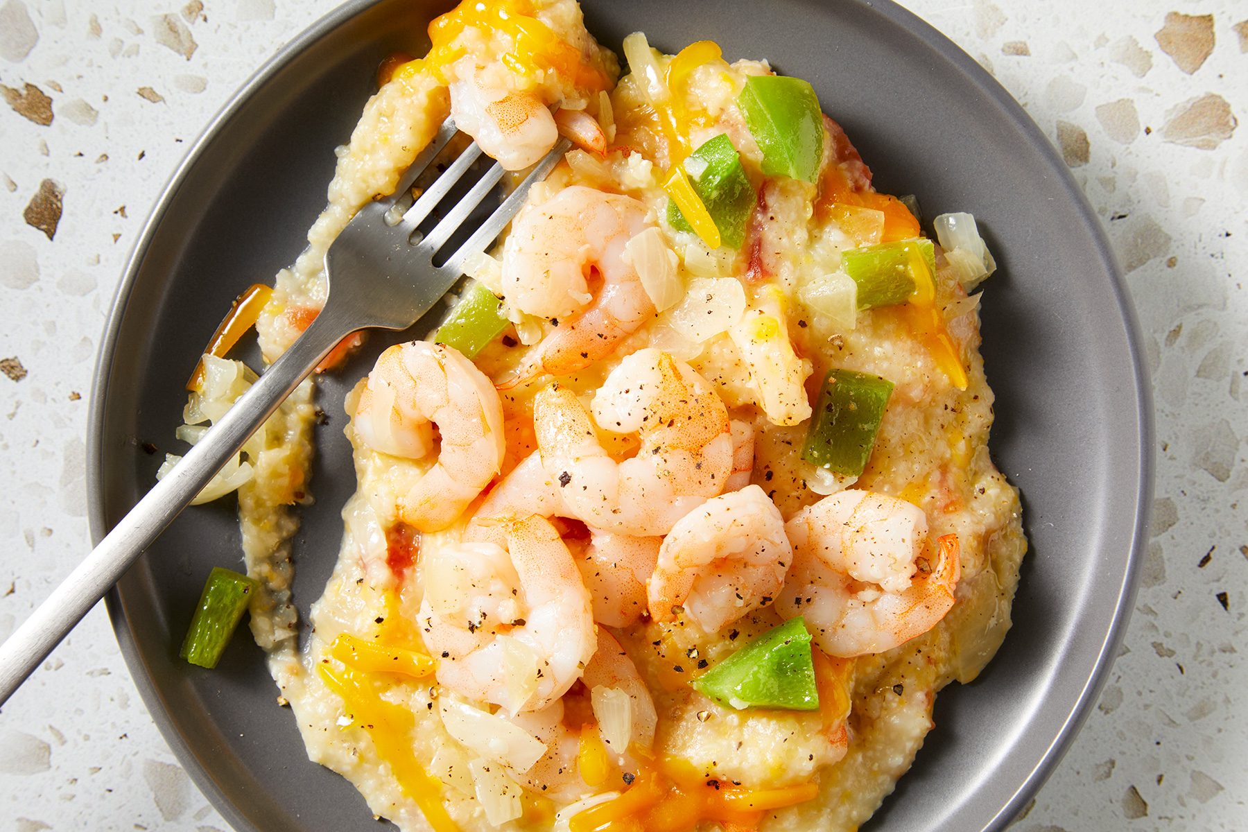 A plate of cheesy grits topped with sautéed shrimp, green bell peppers, and onions is shown. 