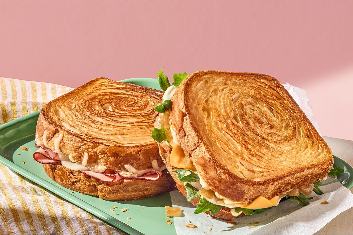 Close-up of two sandwiches on croissant bread, on a green tray with a pink background