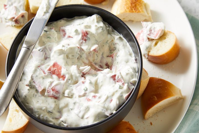 overhead shot of a bowl of Easy Bagel Dip with silver metal spreader placed over the bowl, around the bowl, there are several small pieces of bagel