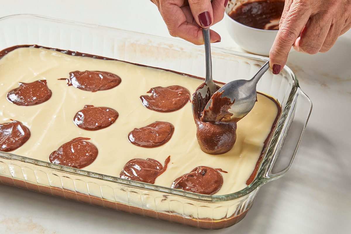 Close shot fo a glass baking dish; Top with remaining brownie batter; all arranged on a marble surface;