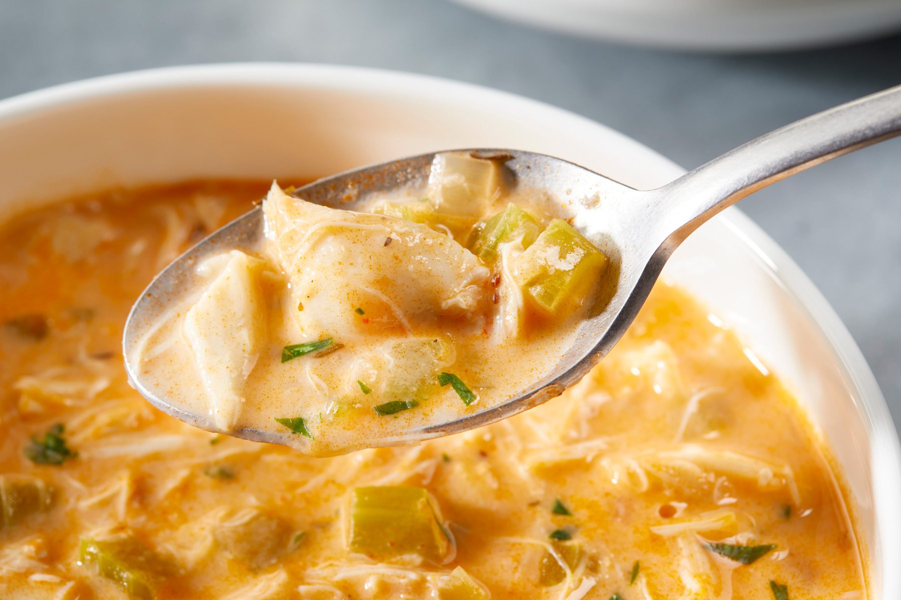 Close-up shot of Homemade Crab Bisque; Garnish with parsley; a large silver spoon lifts a spoonful of bisque; all set on a grey surface;