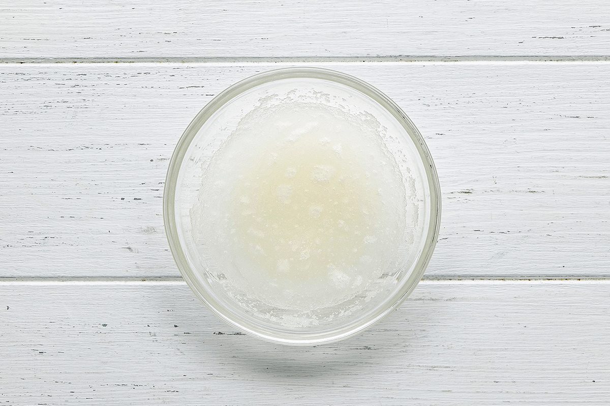 A small glass bowl filled with a white, semi-liquid substance sits on a white wooden surface.