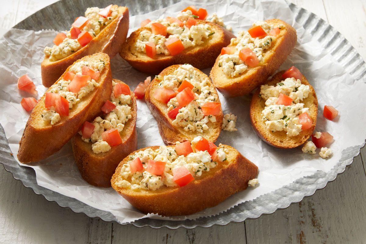 3/4th shot of several pieces of bruschetta arranged on a metallic tray lined with parchment paper;