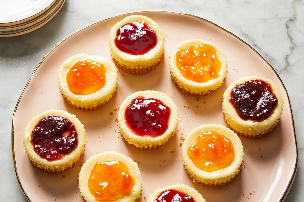 High angle view shot of Jam-Topped Mini Cheesecakes; served them on a big serving plate; small empty plates are nearby; all set on a marble surface