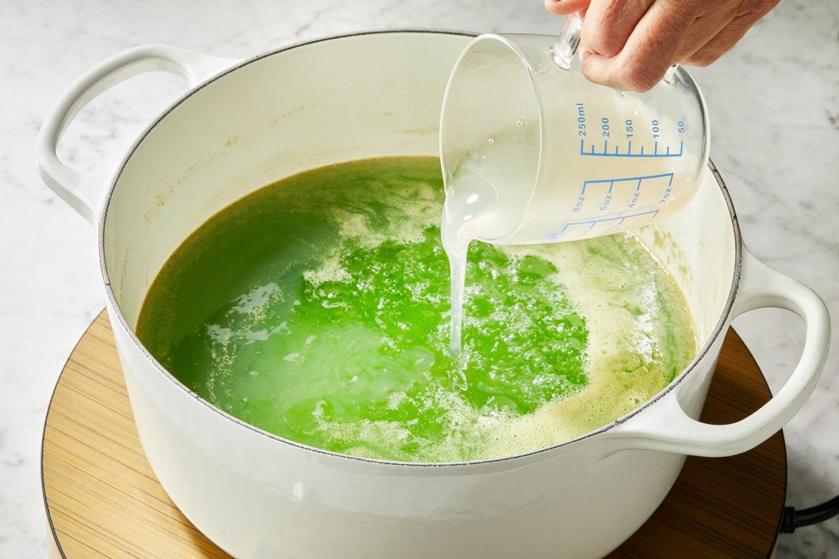High angle view shot of a Dutch oven; combine sugar; lemon juice; food coloring and reserved liquid; Bring to a boil; cook and stir 1 minute; Add pectin; return to a boil. Cook and stir 1 minute; remove from heat; let stand 5 minutes; induction; marble surface;