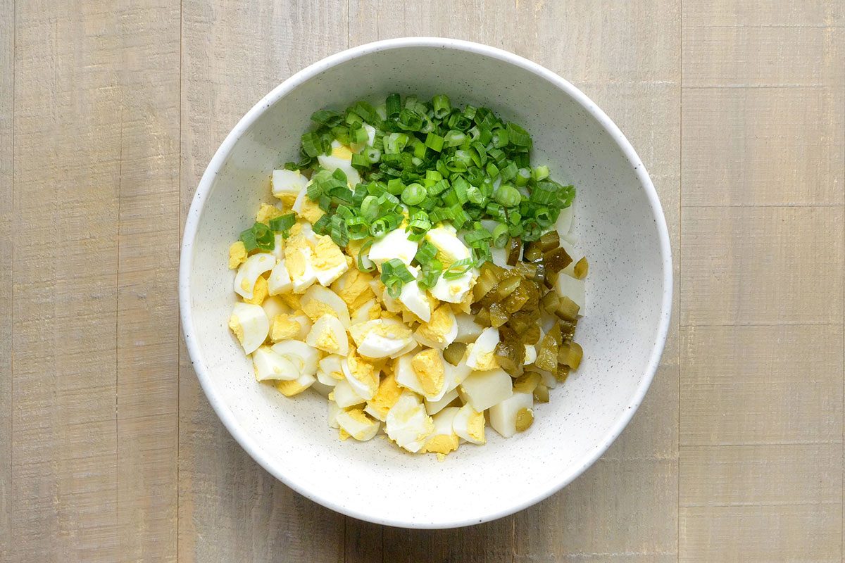 Egges, Onions, pickles are bieng added in a bowl