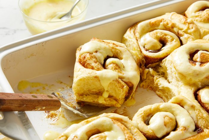 Close-up shot of Best Orange Cinnamon Rolls; in a baking pan; napkin; flat spoon; marble surface;