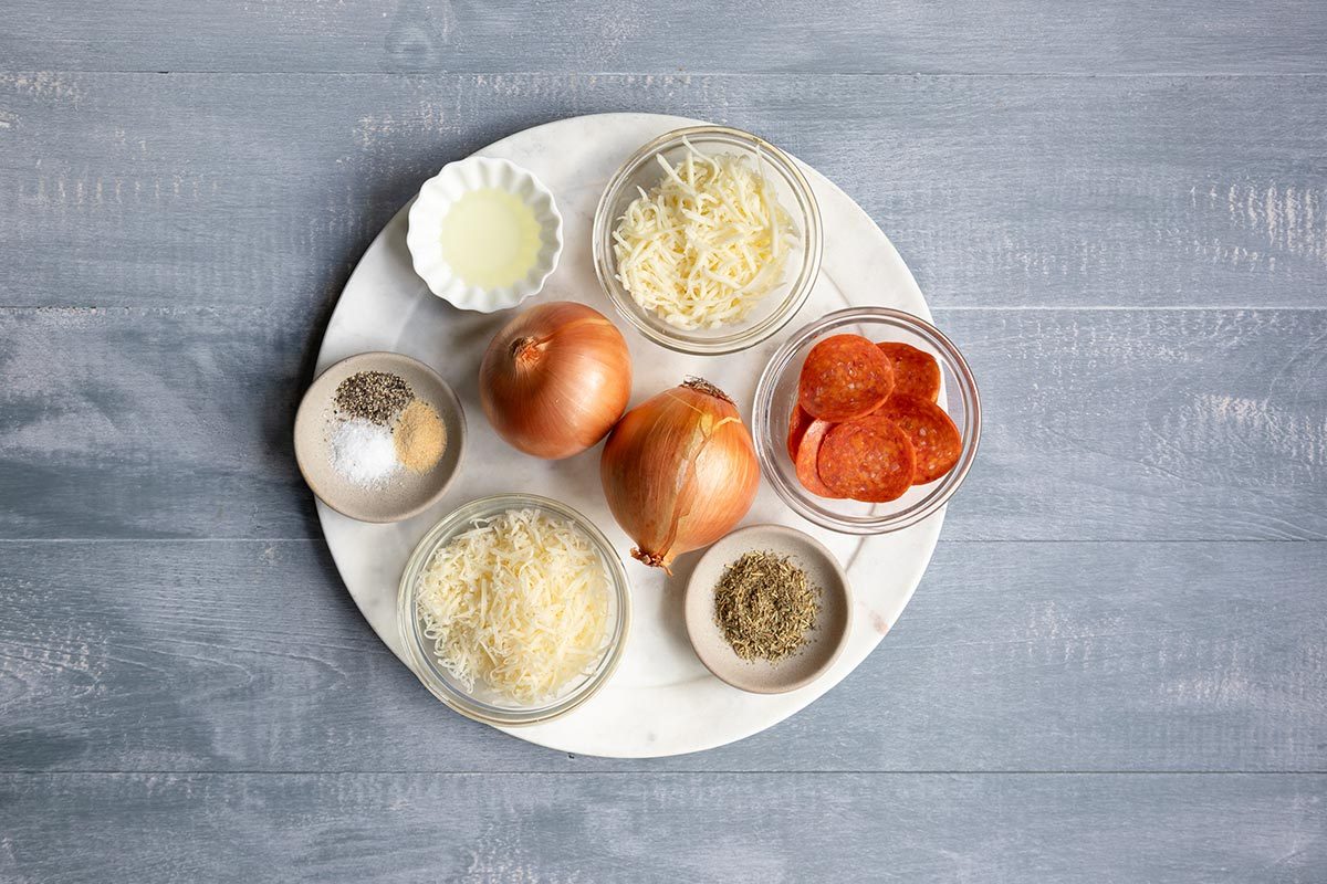 Onions, cheese, pepperoni, oil, and seasonings on a white plate on top of a gray table