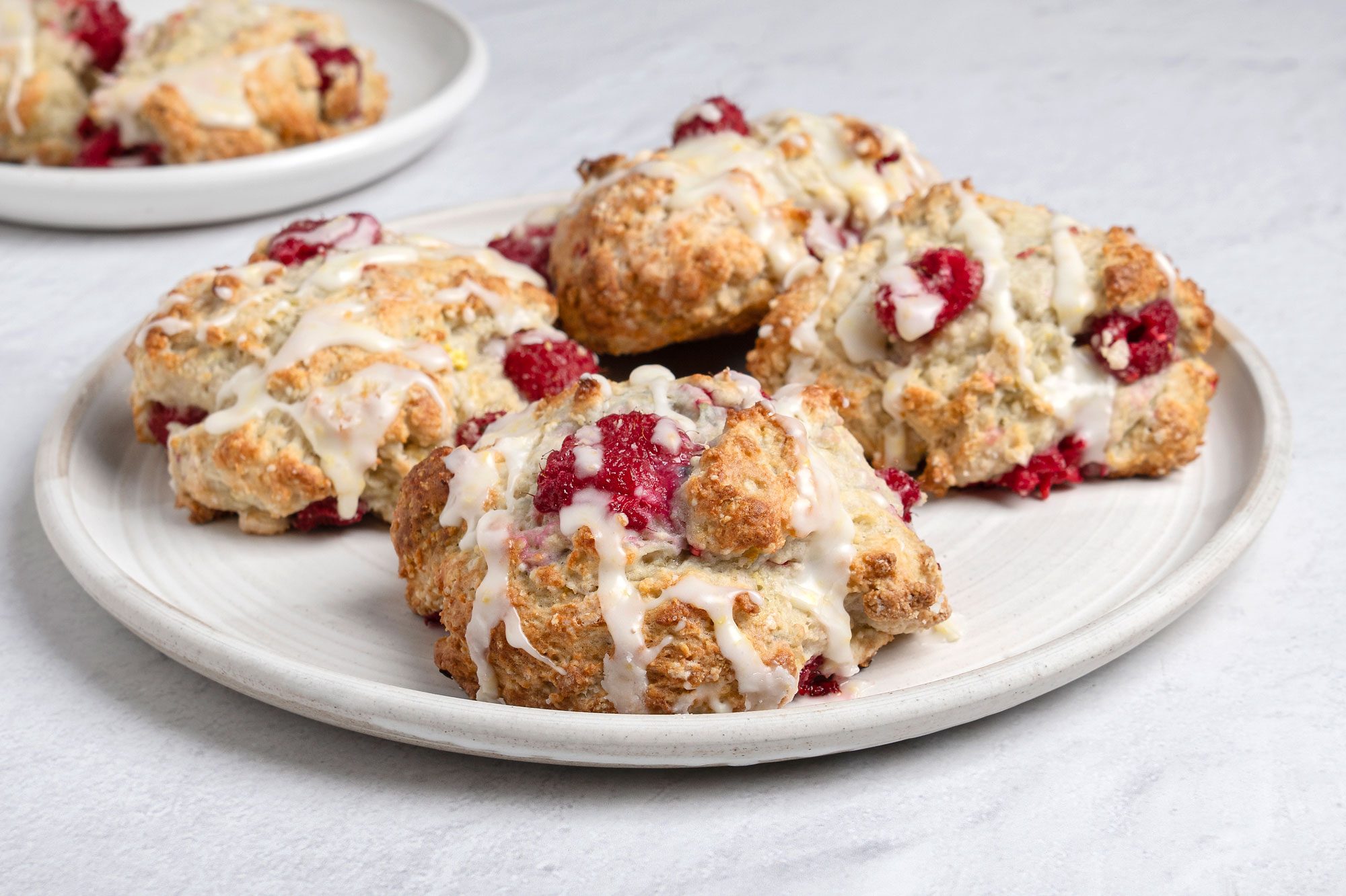 Close-up view shot of Raspberry Drop Scones; served on two round plates; and a napkin; all set on marble surface;