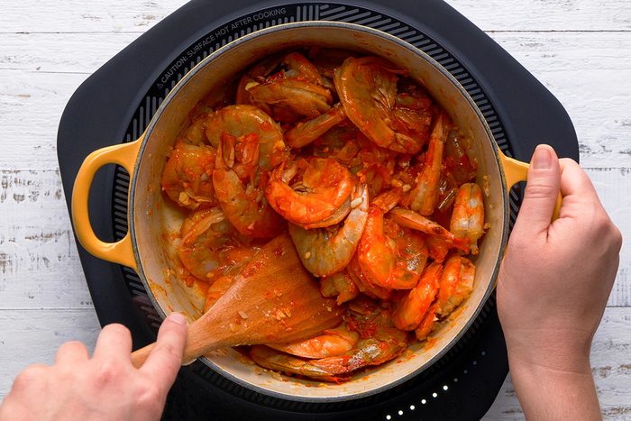 A person using a spoon to stir a pot of food, engaged in meal preparation.