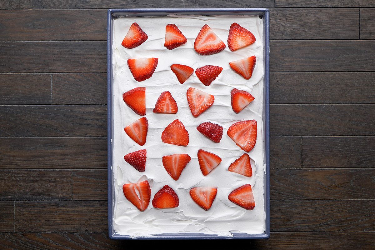overhead shot of a rectangular tray filled with a smooth layer of creamy frosting, decorated with an arrangement of fresh strawberries on top