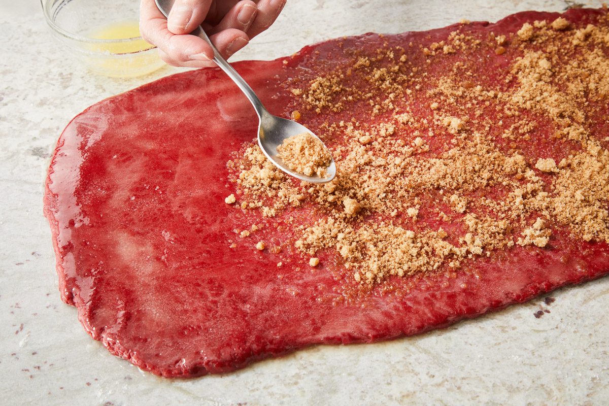 dough surface being sprinkled with brown sugar-cinnamon mixture