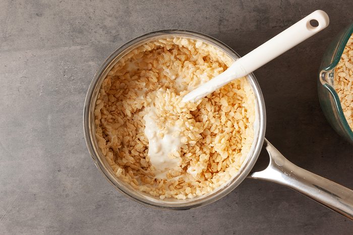 A saucepan filled with cooked rice and a dollop of sour cream being mixed with a white spatula, set on a gray countertop.