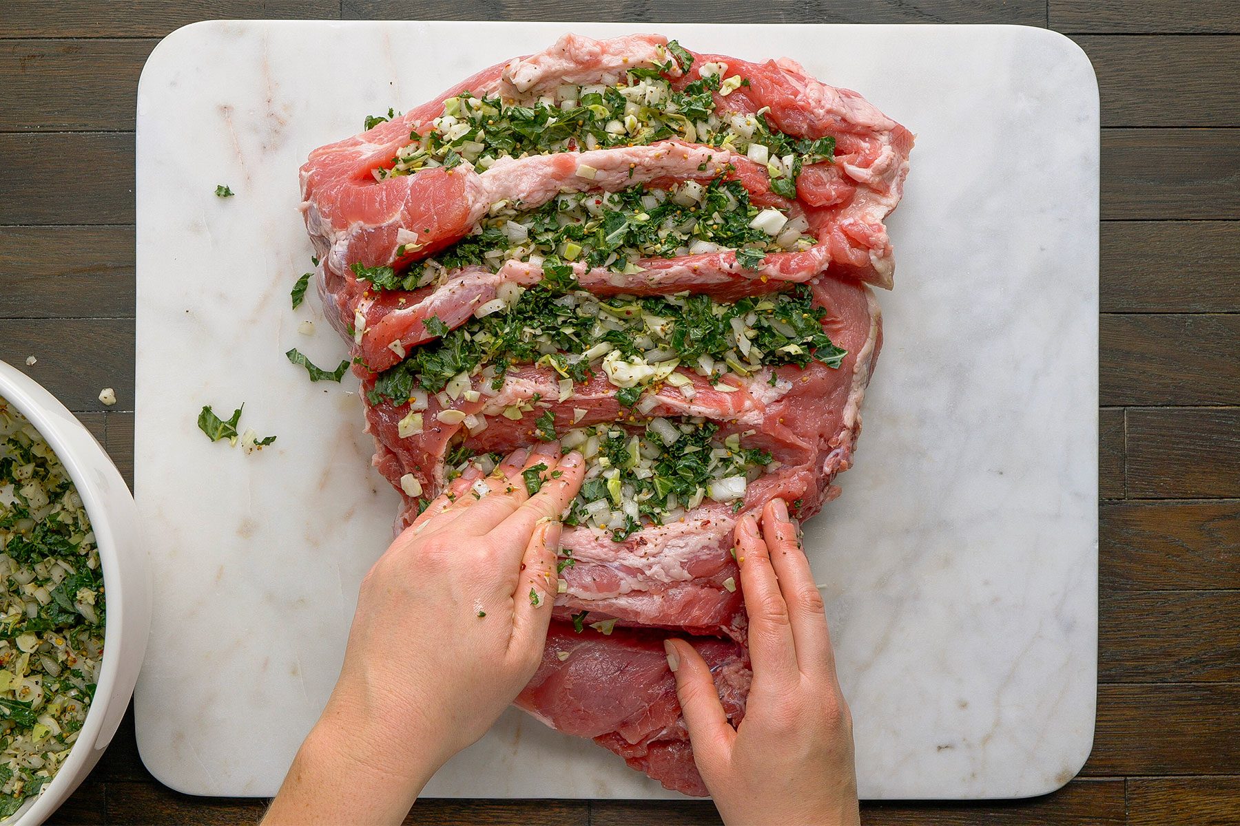 Overhead shot on a white cutting board on a table. Stuff mixture into ham, filling all gaps with your hands.