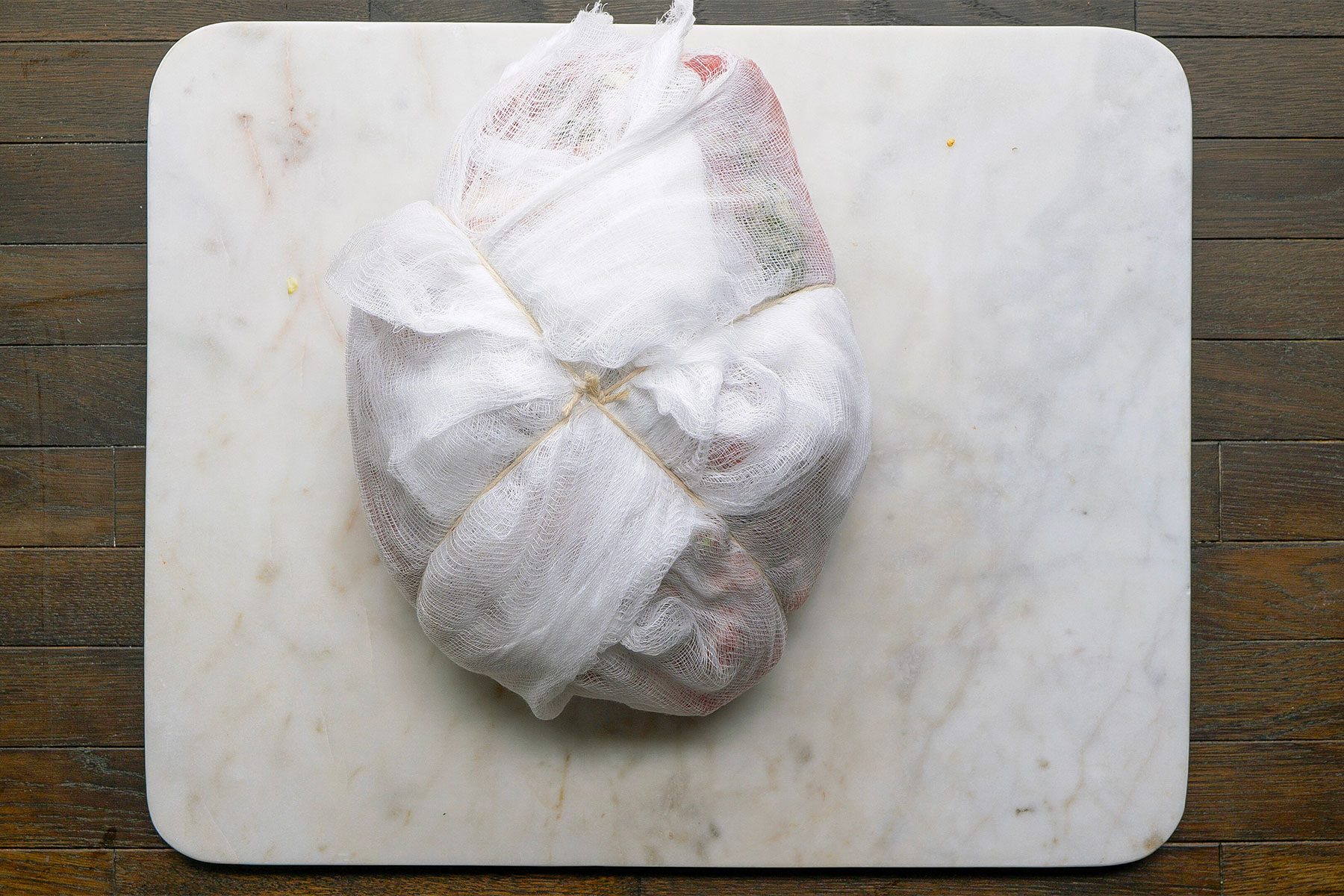 Overhead shot of cheesecloth on a white cutting board on a table. Place the stuffed ham on a double thickness of cheesecloth; bring up corners of cloth and tie tightly with kitchen string.