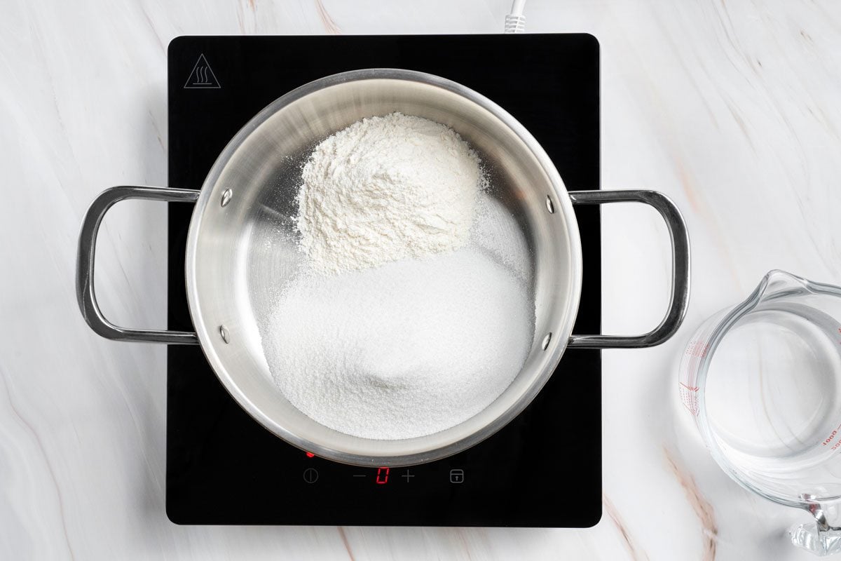 Overhead shot of a large saucepan combine sugar and flour over a induction; arranged on a marble surface;