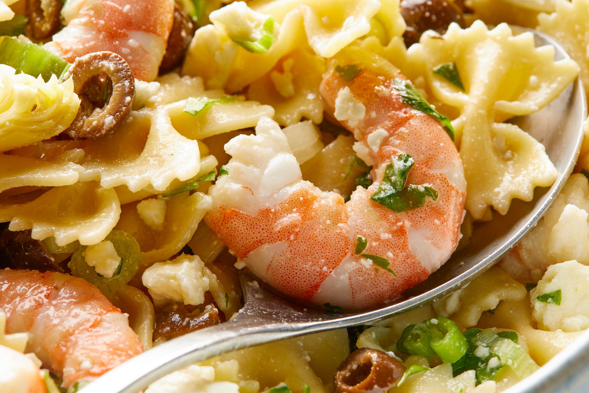 Closeup view shot of Artichoke Shrimp Pasta Salad in a large bowl with a spoon