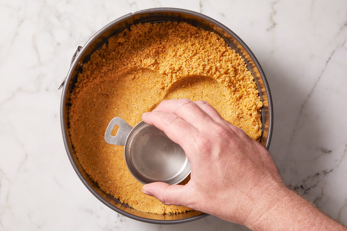 crust mixture being pressed onto the bottom of a springform pan
