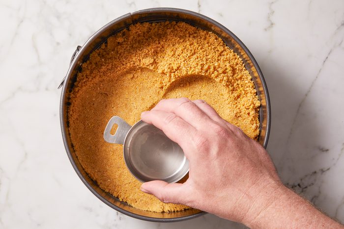 crust mixture being pressed onto the bottom of a springform pan