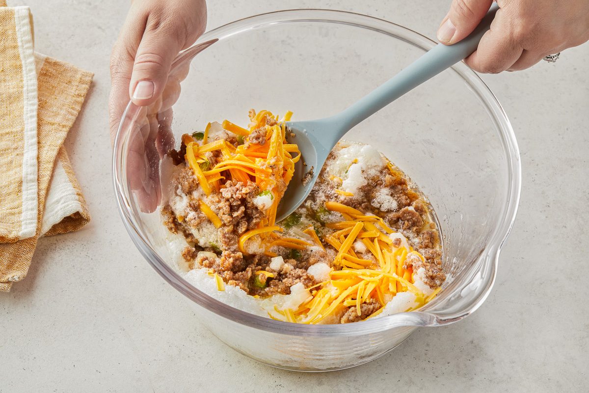Stirring in chopped onion, bell pepper, salt, garlic powder, pepper, cooled sausage and shredded cheese