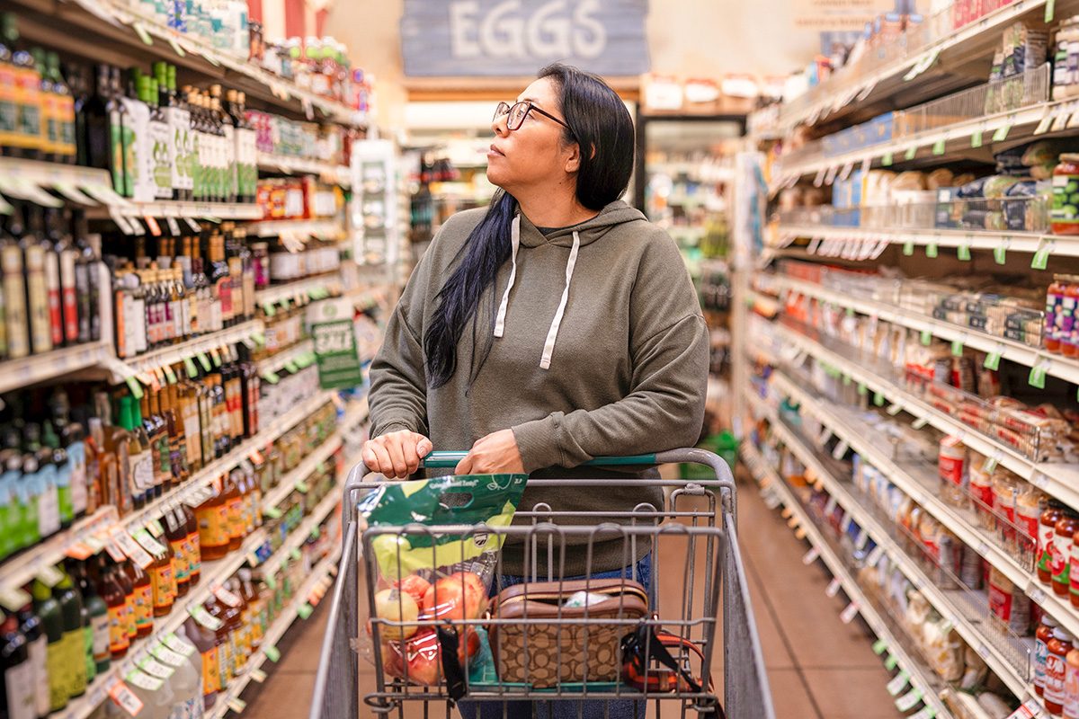 A woman walks down the aisle at the grocery store with her shopping cart