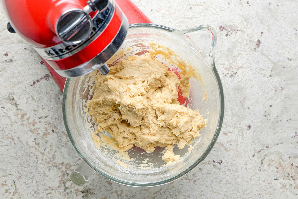 A red stand mixer with a glass bowl contains partially mixed cookie dough on a light-colored countertop.