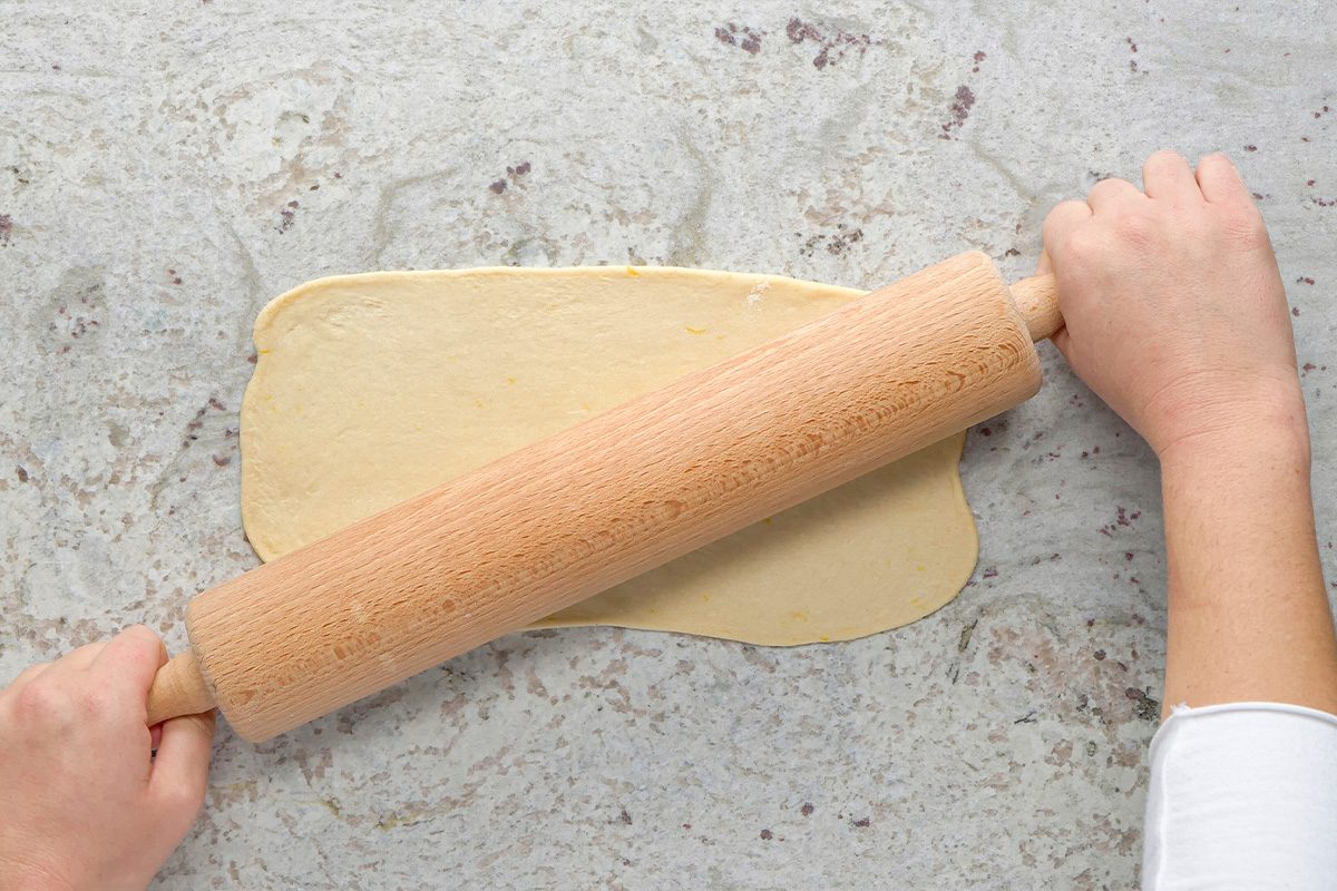 A person uses a wooden rolling pin to flatten dough on a light gray countertop.