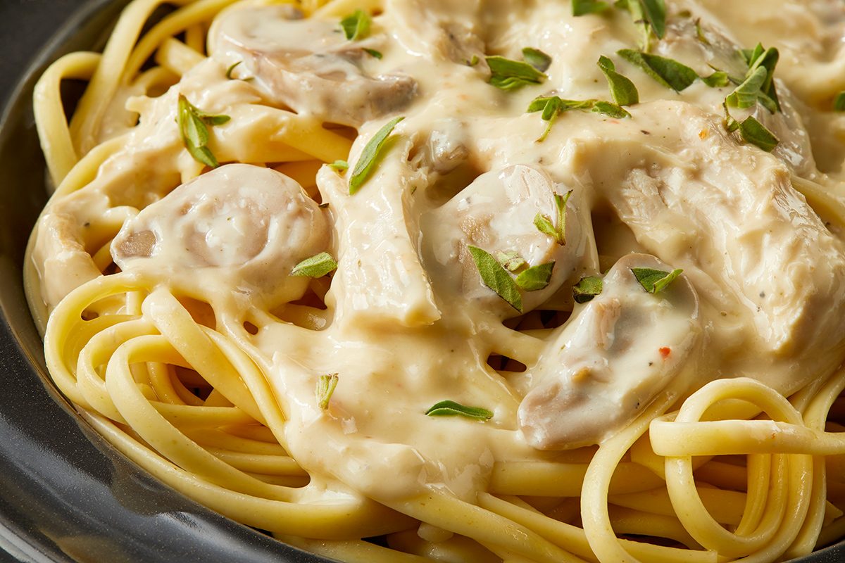 A plate of linguine pasta topped with a creamy white sauce, pieces of chicken, mushrooms, and garnished with chopped fresh herbs.