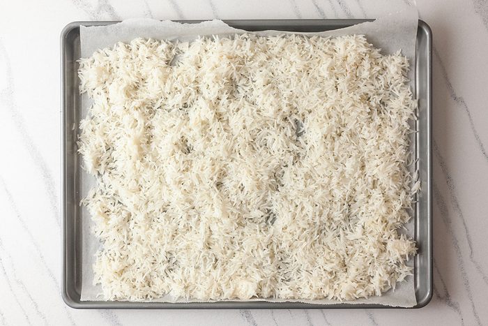 Overhead shot of a baking sheet lined with parchment paper, evenly covered with a single layer of cooked white rice;