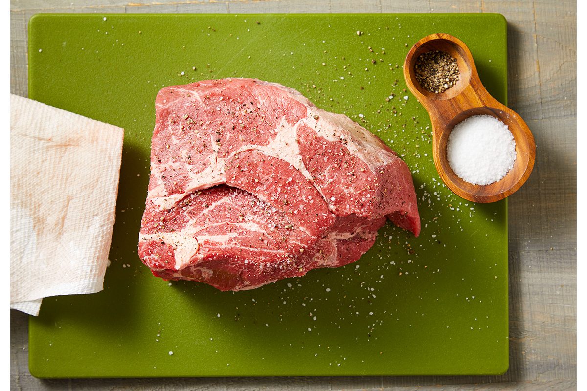 Overhead shot of a raw beef roast on a green cutting board with a small bowl of salt and a napkin beside it.