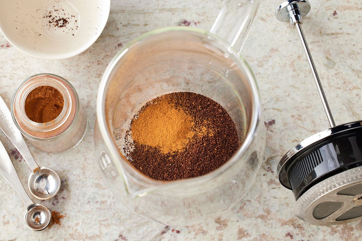 Overhead shot of a glass French press containing ground coffee and spices