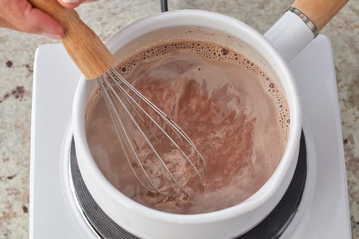 Overhead shot of a hand whisking coffee in a white saucepan on a stovetop