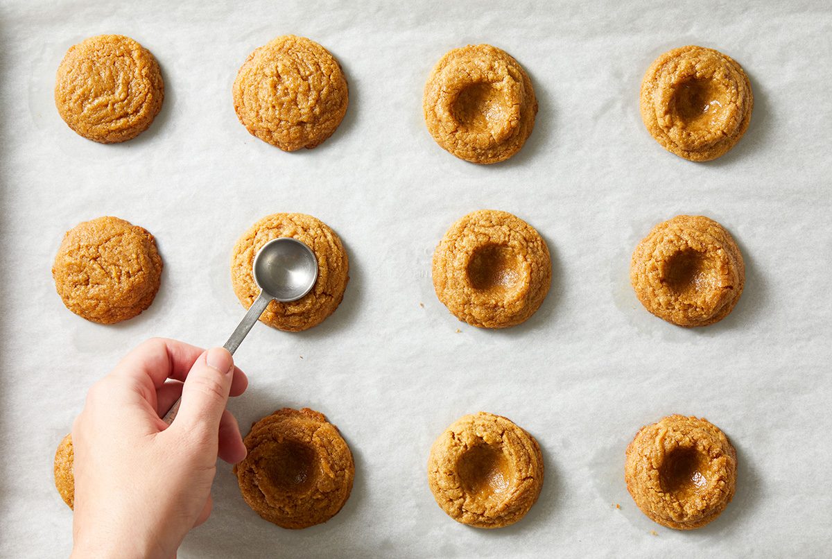 Overhead shot of a hand pressing the center of cookie dough balls with a measuring spoon