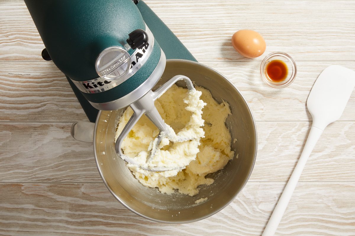 butter and sugar being creamed together in a bowl next to an egg and vanilla extract