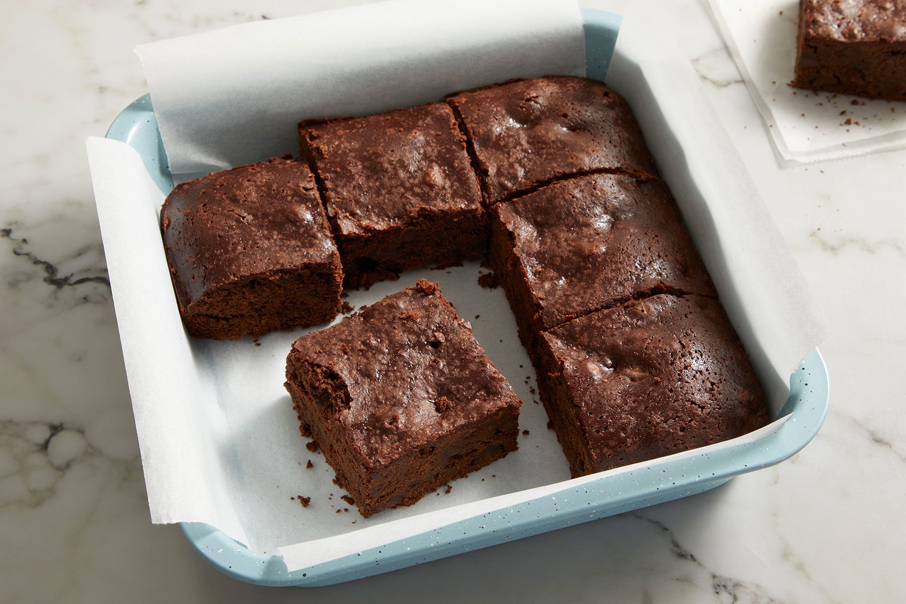 Sourdough Brownies cut into small pieces in a parchment paper lined dish.