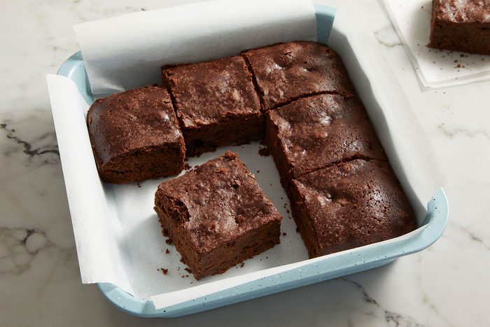 Sourdough Brownies cut into small pieces in a parchment paper lined dish.