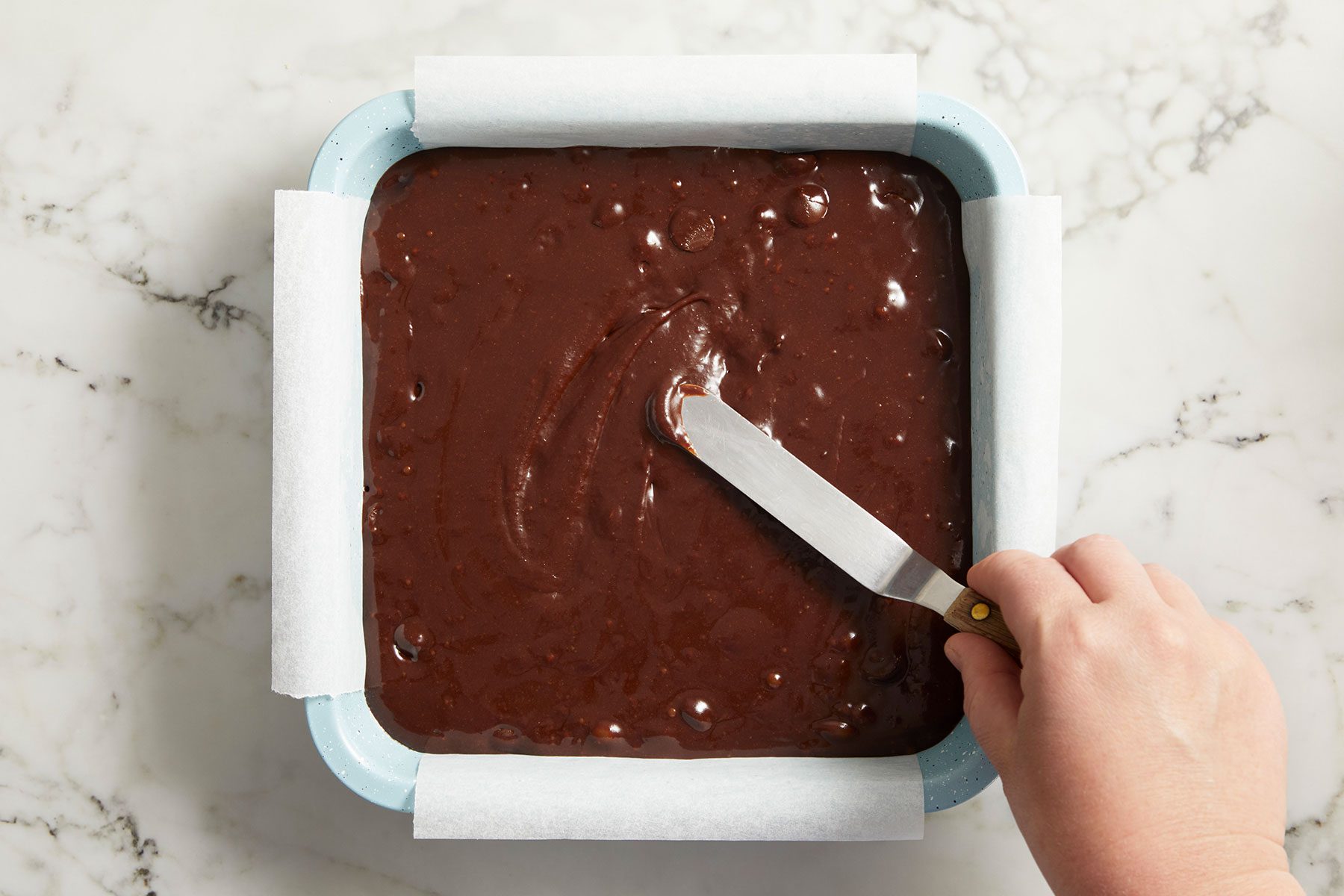 Transfering the brownie batter to the prepared pan and spreading it into an even layer.