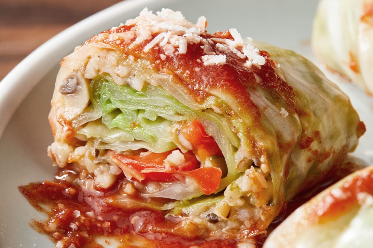 A close-up of a cabbage roll stuffed with vegetables and topped with tomato sauce and grated cheese, revealing colorful layers inside.