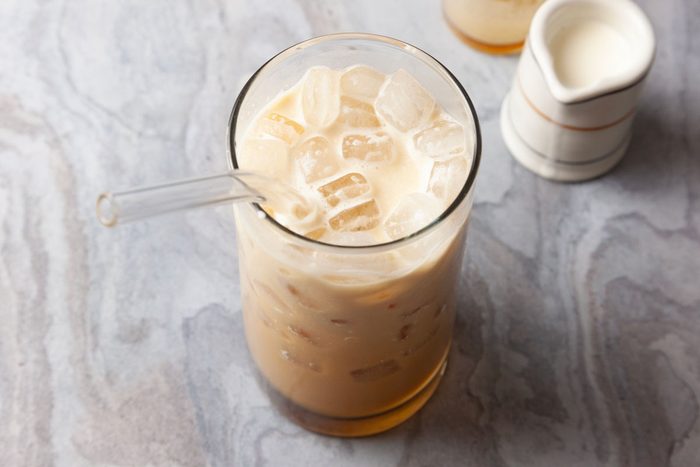High angle shot of Espresso Cream Soda with milk and ice cubes in a glass with a clear straw, placed on gray marble beside a small white creamer.