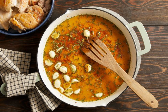Bringing chicken stock, rosemary and thyme to a boil in a pan.