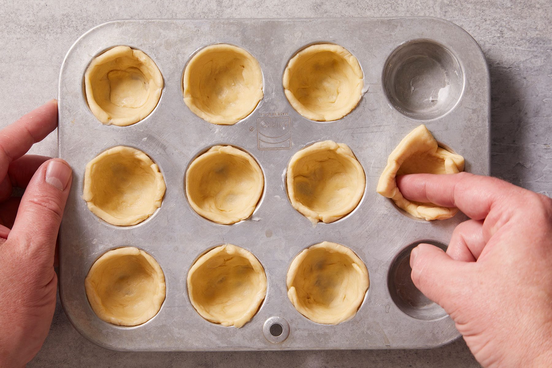 Gently pressing each dough piece into the bottom and up the sides of greased miniature muffin cups.