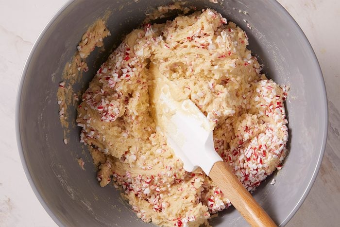 Overhead shot of a mixing bowl filled with biscotti dough studded with crushed peppermint and a spatula resting inside.