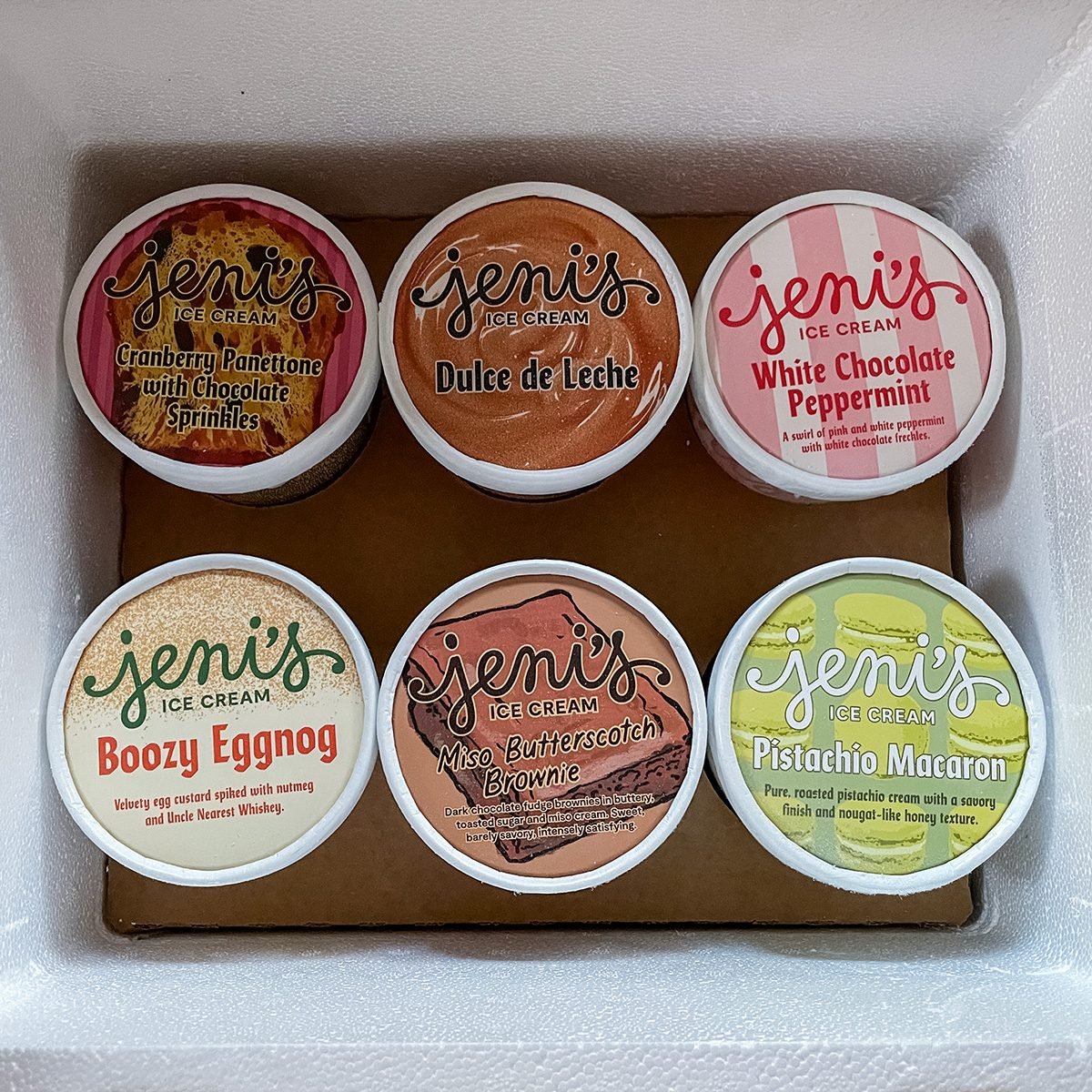 Six Jeni’s Ice Cream pints in a box, with visible labels: Cranberry Punch, Dulce de Leche, White Chocolate Peppermint, Boozy Eggnog, Maple Butterscotch, and Pistachio Macaron.