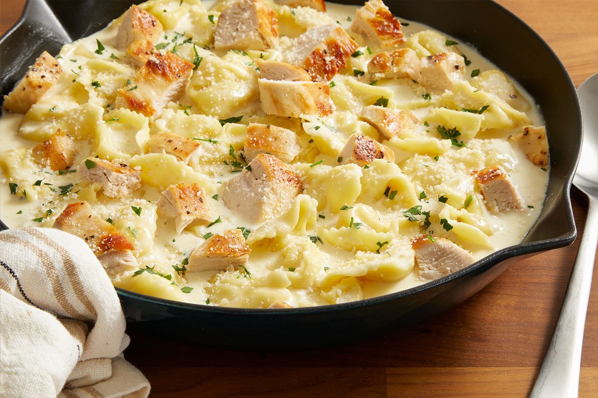 3/4 shot of baked Cheesy Chicken Tortellini Alfredo in a skillet topped with golden melted cheese and parsley.