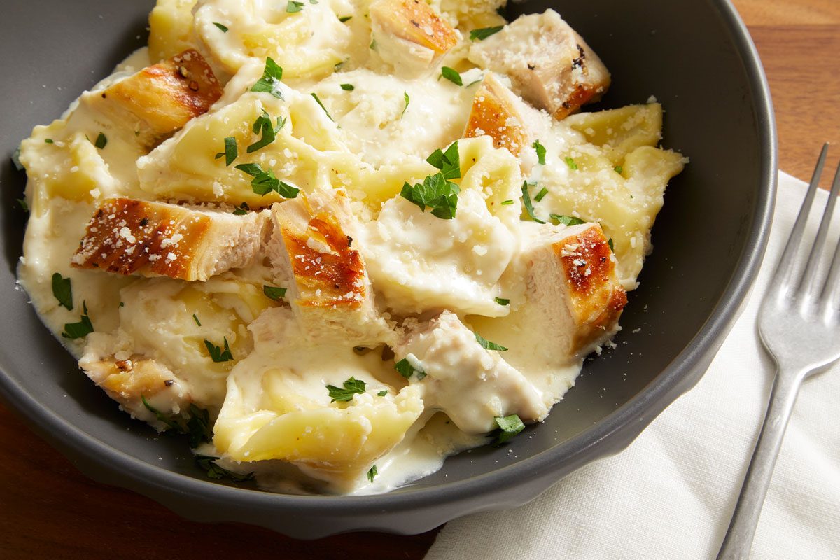 Close-up shot of a bowl filled with Cheesy Chicken Tortellini Alfredo, showing chunks of chicken and creamy sauce.
